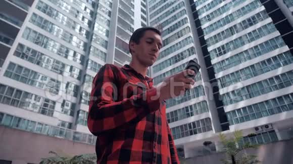 穿格子衬衫的年轻人在城市智能手机上使用应用程序英俊自信的男性在城市智能手机上交流视频的预览图