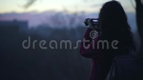 美丽的女摄影师拍摄日落视频的预览图