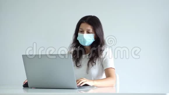这女孩在隔离期间在家工作电晕病毒大流行一个戴手术面罩的女孩在笔记本电脑上工作为她带来咖啡视频的预览图
