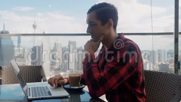 一位自信的商人在一台笔记本电脑上工作在一座摩天大楼屋顶的咖啡馆喝咖啡背景是一台笔记本电脑视频的预览图