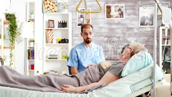 一位男医生和躺在养老院病床上的生病的老太太谈话视频的预览图