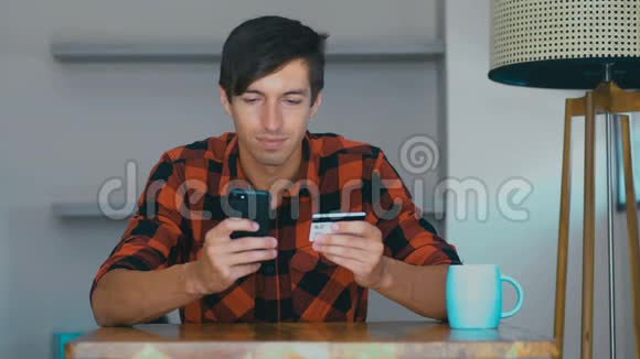 有信用卡和电话的人年轻男性坐在家里的办公桌上通过互联网支付在线费用视频的预览图