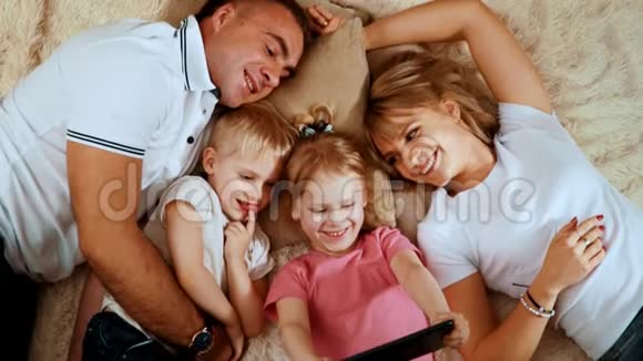 幸福的家庭孩子们躺在毯子上他们看着女儿拿着的平板电脑视频的预览图