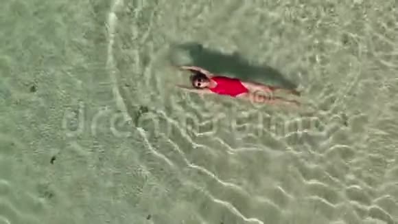 就在幸福微笑的顶部身穿红色比基尼和太阳镜的女人在清澈的海水中游泳视频的预览图