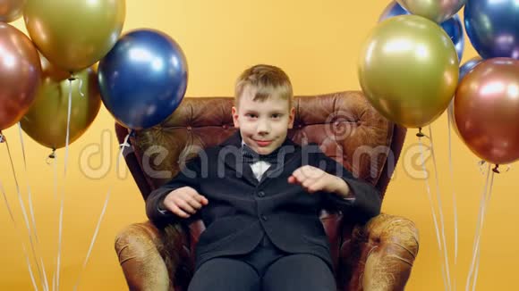 男孩交叉双臂胸脯坐在椅子上黄色背景上有气球视频的预览图