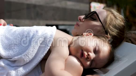 美丽的年轻母亲和她可爱的小女儿睡在开放的游泳池旁视频的预览图