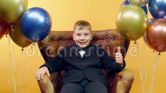 有趣的男孩表现得像一个标志坐在皮椅上有着五颜六色的气球视频的预览图