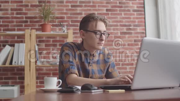 一个穿着鼻子的嬉皮士正在笔记本电脑前工作对着相机微笑办公室的年轻上班族视频的预览图