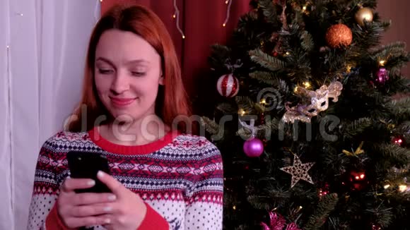 圣诞树附近的女人漂亮的女性使用手机获得新年祝贺祝你快乐视频的预览图