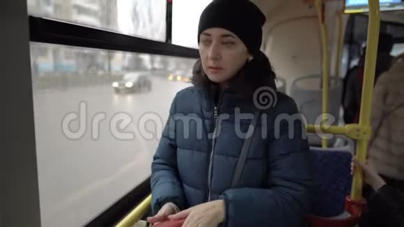 一个悲伤的成年女孩站在公共汽车里面的一扇窗户前从钱包里掏出一张信用卡窗外视频的预览图