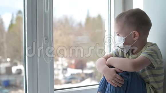 悲伤的孩子戴着保护性医疗面具坐在窗台上看着窗外检疫呆在家里病毒视频的预览图