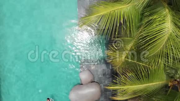 年轻女子在豪华游泳池和棕榈树游泳时仰面漂浮在比基尼上假期概念视频的预览图