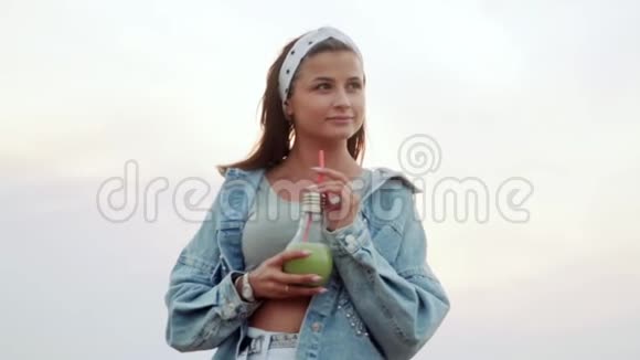 一个好女孩站在屋顶上慢慢地通过一个管子喝一杯美味的酒精鸡尾酒慢动作夏天视频的预览图