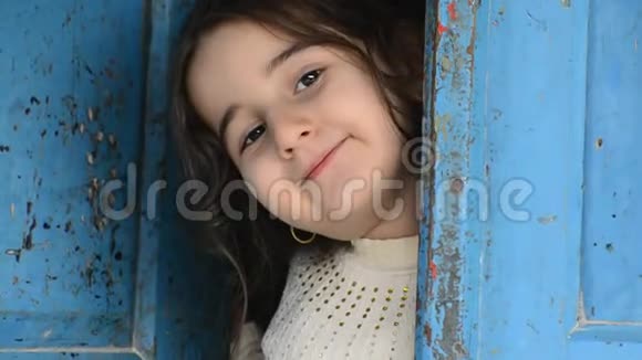 蓝色木门后一个小女孩的肖像视频的预览图