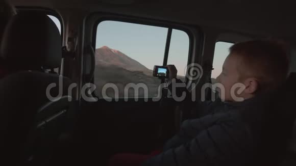 一个男孩在驾驶汽车的后座上拍摄山景视频的预览图