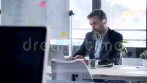 英俊的商人坐在办公室里用笔记本电脑工作视频的预览图