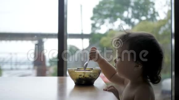可爱的学步女孩吃健康燕麦与鳄梨和猕猴桃早餐视频的预览图