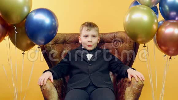 严肃的男孩用手坐在椅子上用黄色的气球表示不喜欢的迹象视频的预览图