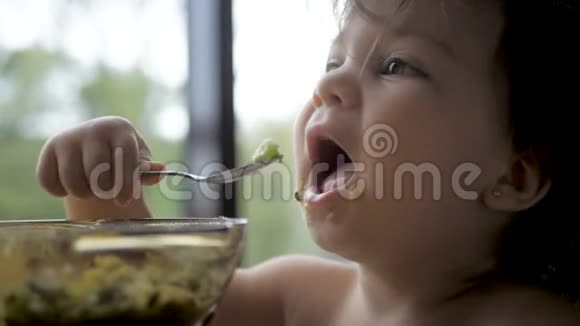 可爱的学步女孩吃健康燕麦与鳄梨和猕猴桃早餐视频的预览图