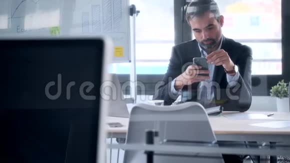 英俊的商人在办公室工作时用智能手机发送信息视频的预览图
