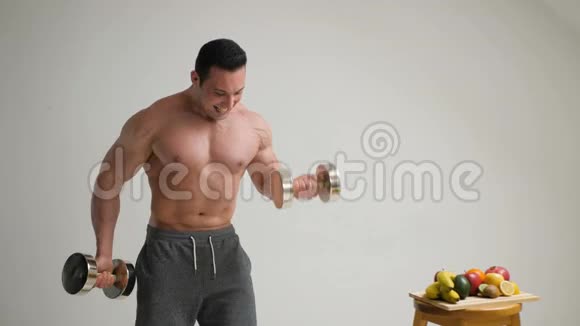 英俊的肌肉男在水果的背景下将二头肌举起来视频的预览图
