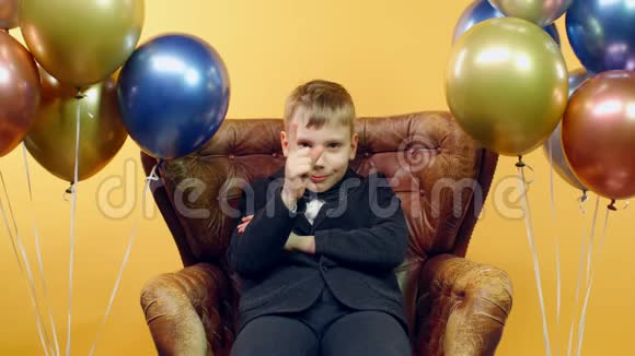 穿夹克衫的滑稽男孩在黄色背景下坐在椅子上摇动手指视频的预览图