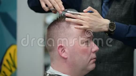 理发店的男式理发大师用剪刀剪一个金发男人的特写镜头视频的预览图