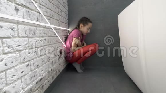 一个悲伤的小女孩坐在房间的角落里坐在沙发后面的地板上抱着她的膝盖擦拭着视频的预览图