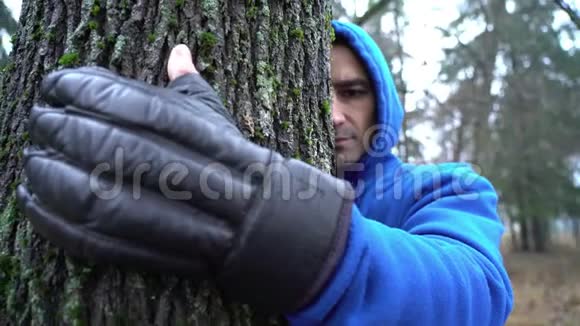 戴着拳击手套的年轻人拥抱森林中的树热爱大自然成年白种人男性环保手视频的预览图