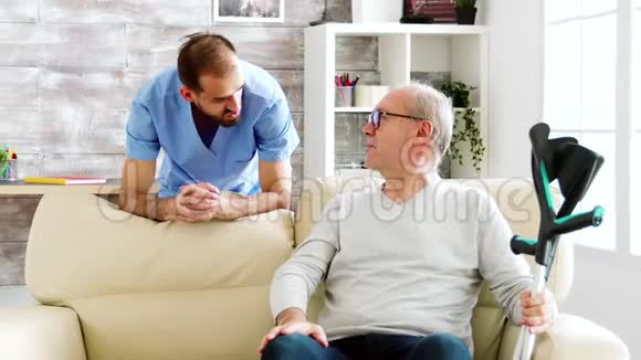 一位老人在舒适的养老院里和一位男护士交谈视频的预览图