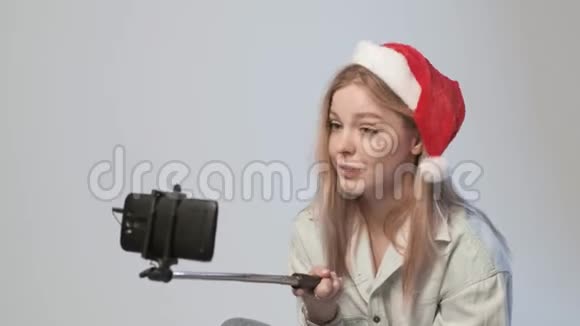 戴着圣诞帽的年轻女孩用智能手机录制自拍棒视频视频的预览图