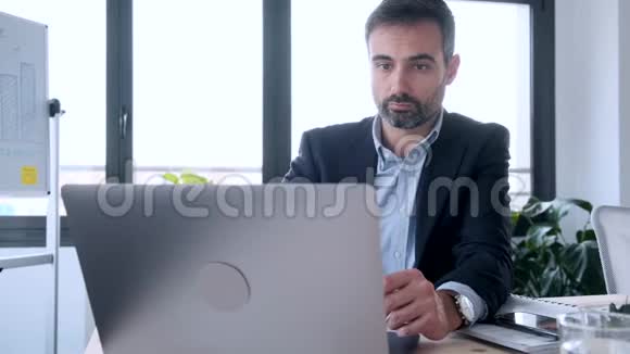英俊的商人坐在办公室里用笔记本电脑工作视频的预览图