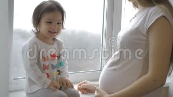 可爱的小女孩拥抱着她美丽的怀孕妈妈肚子微笑着视频的预览图