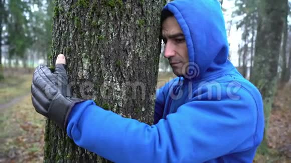 戴着拳击手套的年轻人拥抱森林中的树热爱大自然一个人试图治疗他的悲伤并消耗能量视频的预览图