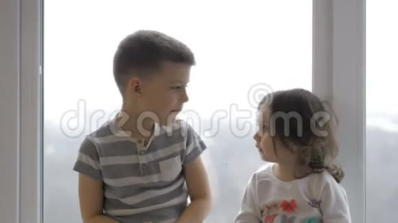 可爱的小男孩和女孩坐在家里的窗台上吃苹果视频的预览图