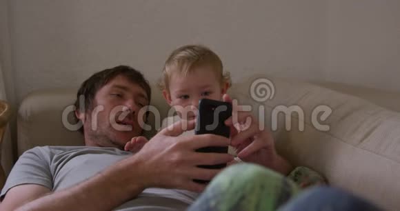 白种人看着智能手机带着孩子在家视频的预览图