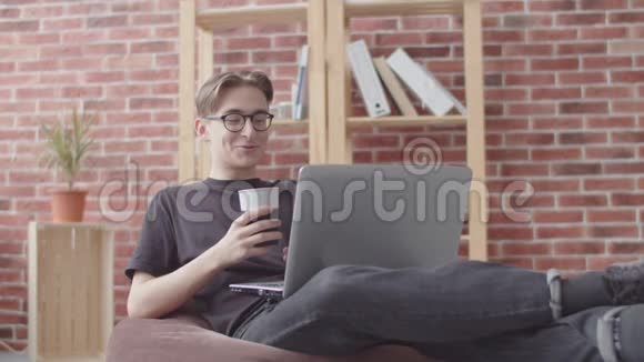 自由职业者通过笔记本电脑通过视频聊天交谈并看相机一个年轻人坐在包椅上交流视频的预览图