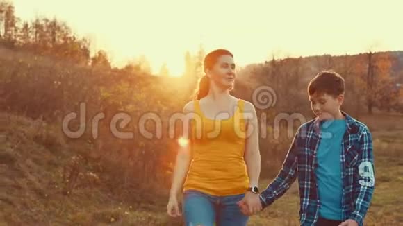 母亲和儿子一起走在草坪上带着美丽的夕阳感受着爱的家庭生活视频的预览图