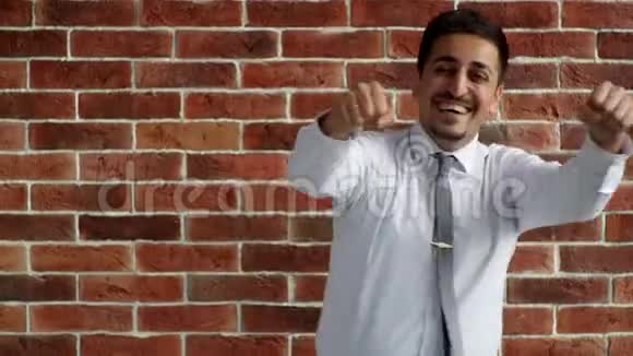 一个穿衬衫的人正在砖墙上跳舞快乐的阿拉伯企业家为胜利而欢欣鼓舞视频的预览图