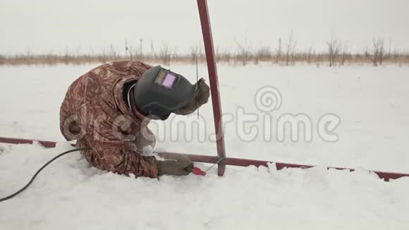 一名专业焊工在雪地里跪着时焊接金属框架穿着冬装手套和电焊面罩的人视频的预览图