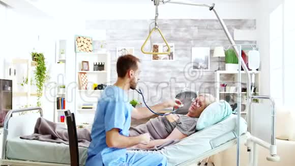 男护士检查躺在病床上的一位生病的老太太的心跳视频的预览图