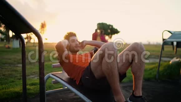 健身男子在公园的健身器材上做仰卧起坐运动以适应腹肌减肥胃脂肪视频的预览图
