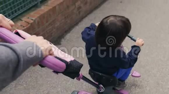 一个小女孩在玩玩具自行车而她的母亲推着她前进视频的预览图