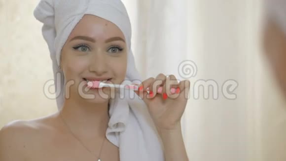 年轻漂亮的女孩在浴室的镜子前用毛巾刷牙视频的预览图