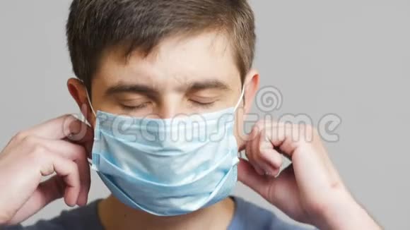 一位年轻医生的脸在灰色的工作室背景上戴上外科口罩医学和健康的概念检疫视频的预览图