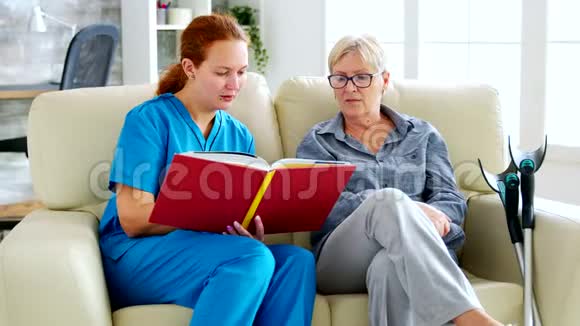 在养老院为一位退休老年妇女读一本书的白人女性助手视频的预览图