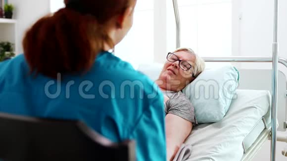 在养老院里躺在床上的老太太和一位女护士谈话视频的预览图