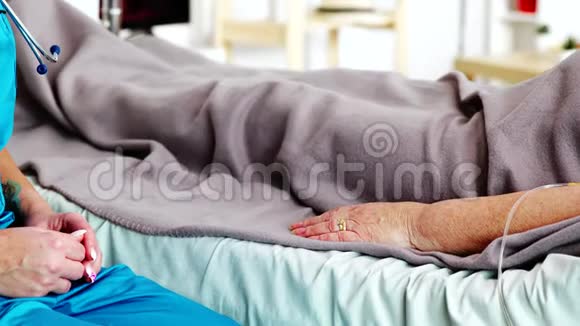 一名年轻的白种人助手抓住躺在病床上的老太太的手视频的预览图