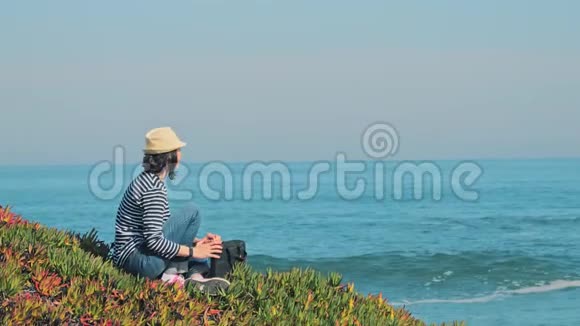 戴草帽的女人会在美丽的海岸线上使用笔记本电脑视频的预览图