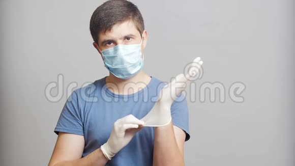 戴着幽默的外科口罩戴着灰色背景的无菌手套狡猾地搓手概念医学笑话奇怪的医生视频的预览图